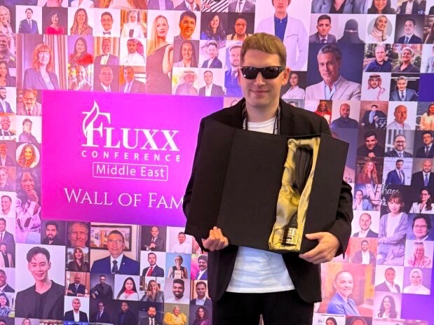 Professional standing at an international conference holding an award in front of a recognition display.